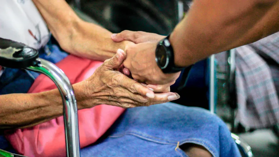 Family member gently holding the hand of a senior seated in a chair