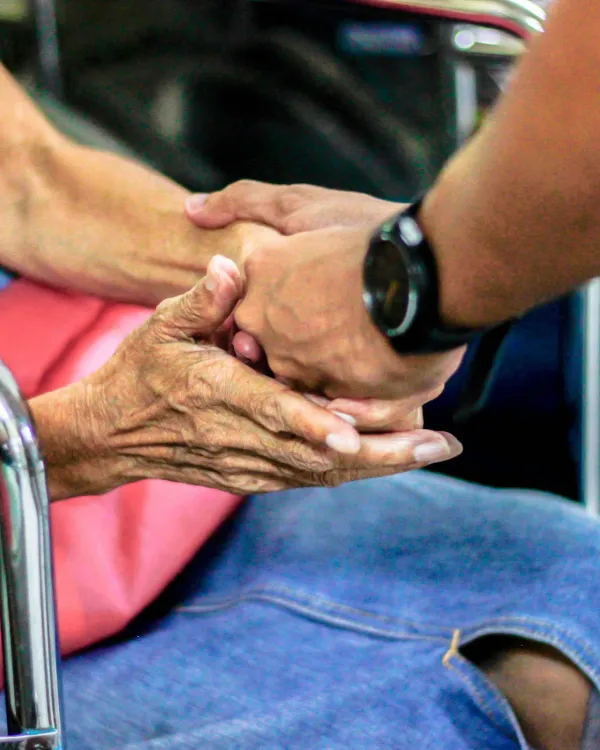 Family member gently holding the hand of a senior seated in a chair