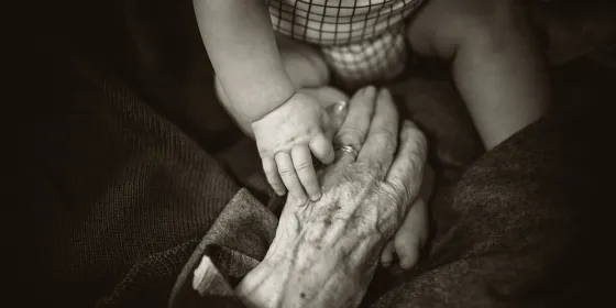 Senior woman gently holding an infant's hand